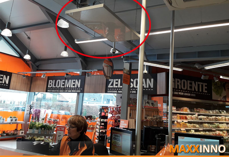 plafondverwarming in een commerciële hal met hangend infraroodpaneel boven werk- en klantzones
